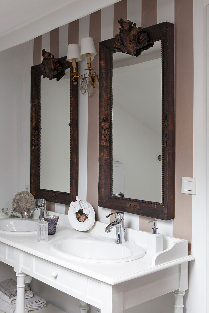 White washstand with twin sinks below two mirrors decorated with antique-style, ornate papier mâché frames