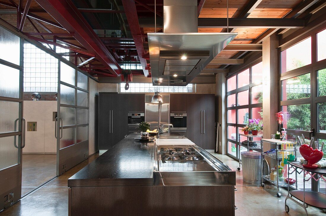 Moderne Designerküche in Loft, vorne Kücheninsel, Wand mit Einbaugeräten im Hintergrund und Blick in Halle