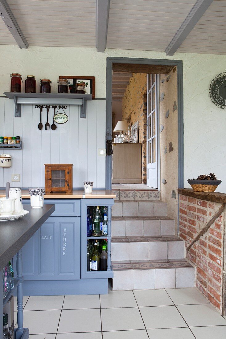 Blau-graue Küche im Landhausstil, mit Durchgang und Treppenstufen zum Wohnbereich
