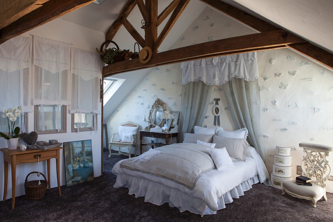 Romantisch eingerichtetes Schlafzimmer; Spitzenkissen auf Doppelbett vor Vorhang mit Schabracke im Dachgeschoss