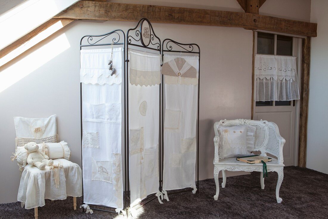 Metal screen covered in white lacy fabric next to chairs with vintage-style accessories