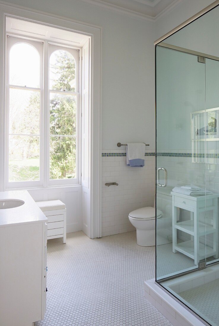 Bad in Weiß, Waschtisch mit integriertem Becken im Unterschrank, gegenüber Duschkabine aus Glas, weiße Mosaikfliesen auf Boden