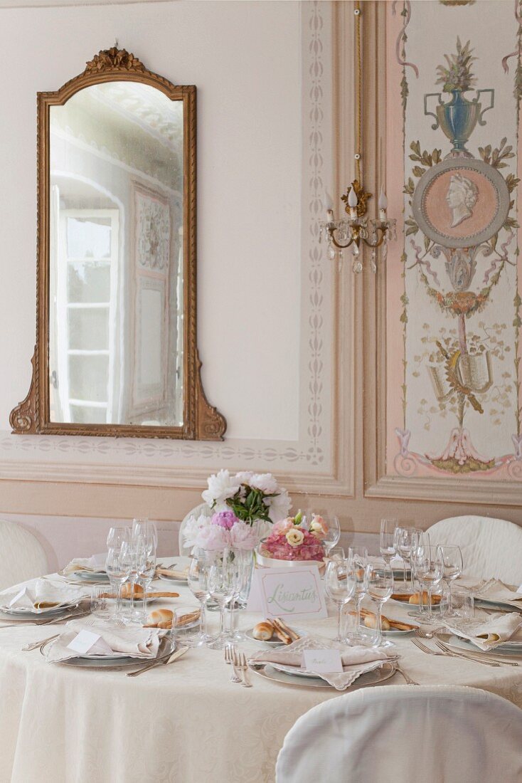 Festlich gedeckter Tisch in elegantem, traditionellem Ambiente, bemalte Paneele und Spiegel mit geschnitztem Rahmen an Wand