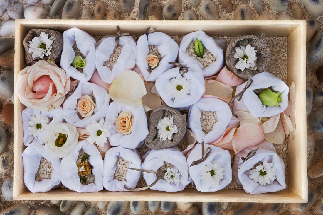 Blüten in weissen Stoffsäckchen, in einer mit Reis gefüllten Holzkiste