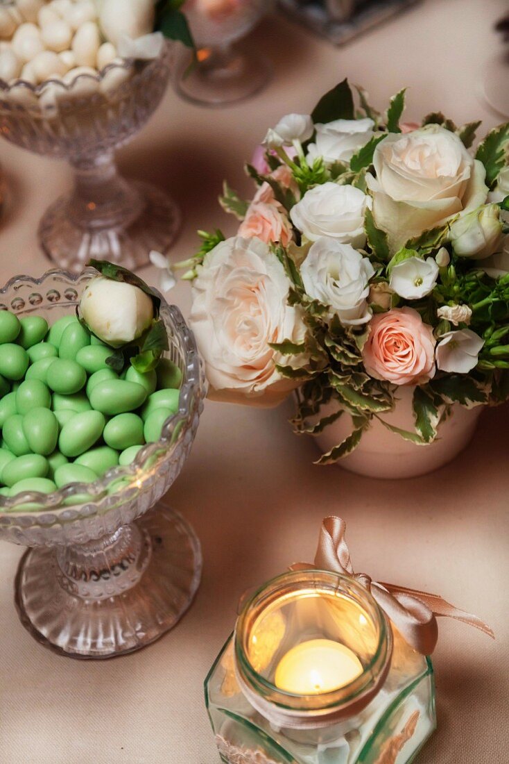 Schale mit grünen Hochzeitsmandeln, festlichem Blumengesteck und Windlicht