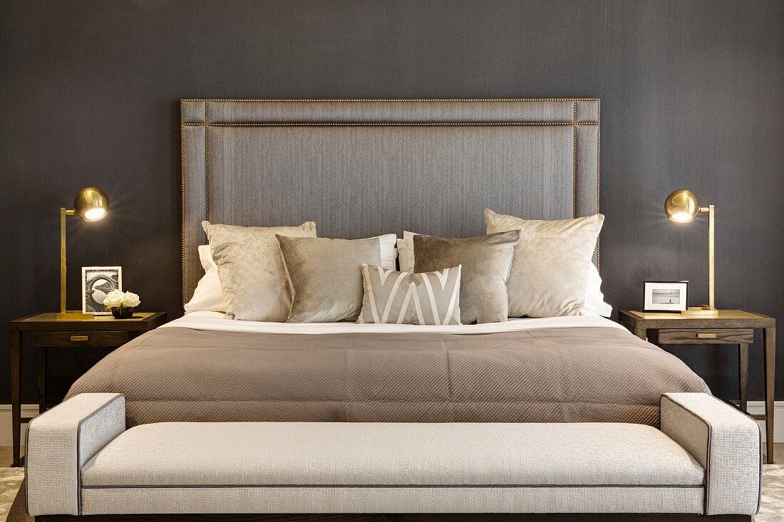 Polsterbank an Fussende eines Doppelbettes mit hohem Kopfteil an Wand, seitlich Messing Nachttischleuchten, in elegantem Schlafzimmer