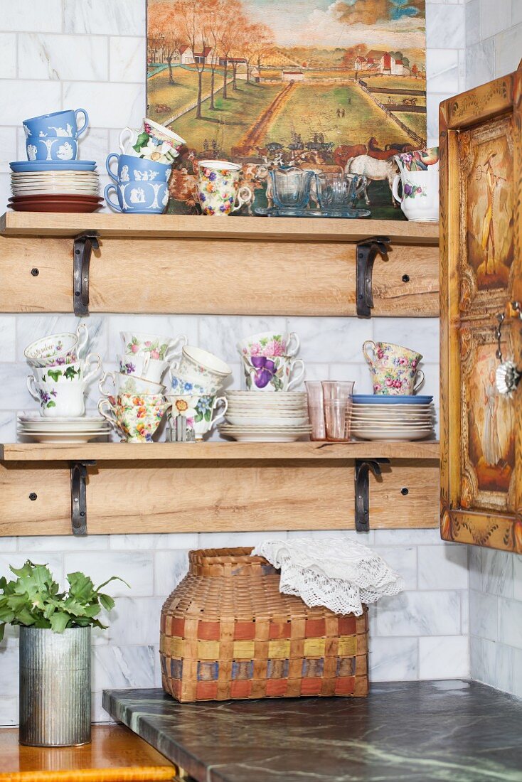 Verschiedene Tassen mit Untertellern auf Holzregal in rustikaler Küchenecke