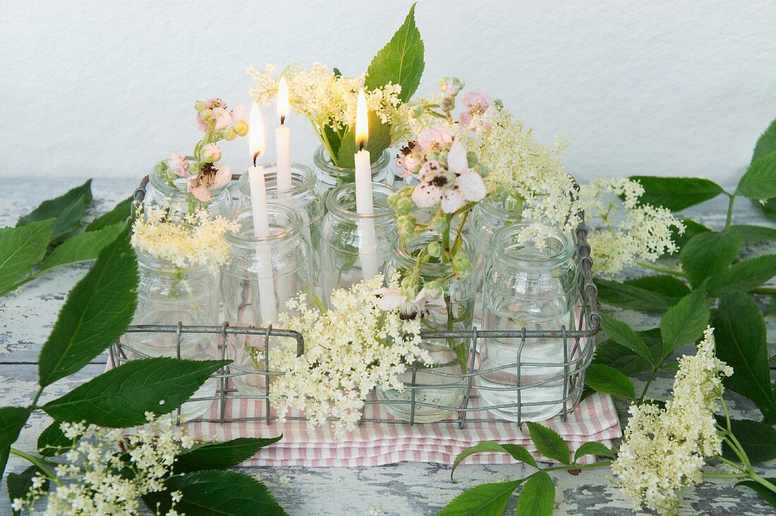 Gläser mit Kerzen, Holunderblüten und Brombeerblüten in Metallkorb