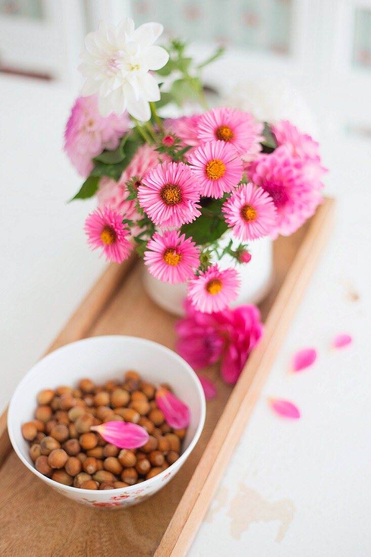 China bowl of hazelnuts and pot of daisies on wooden tray