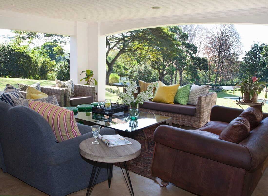 Sitzbereich mit verschiedenen Sofas und Rattanmöbeln auf überdachter Terrasse mit Blick in den weitläufigen Garten