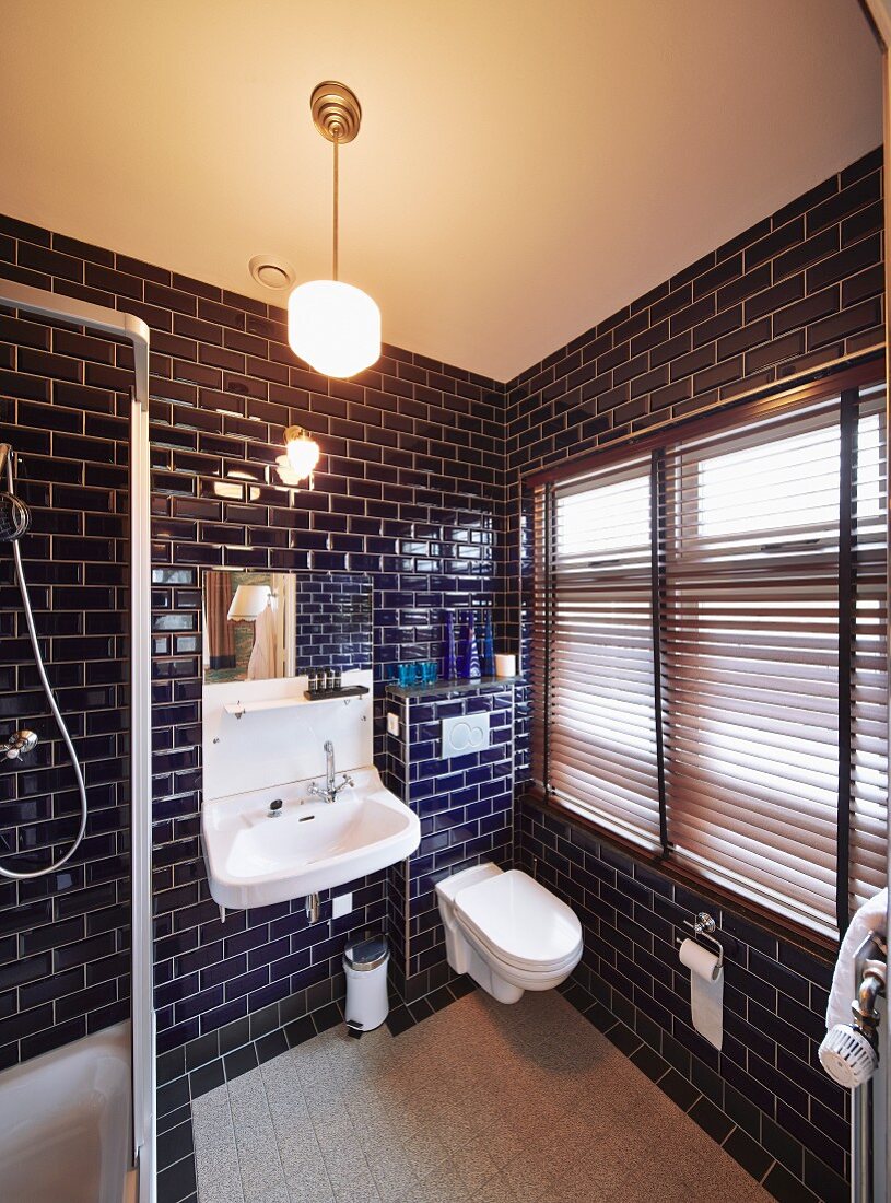 Bathroom with dark blue tiles, white fittings and closed louvre blinds on window