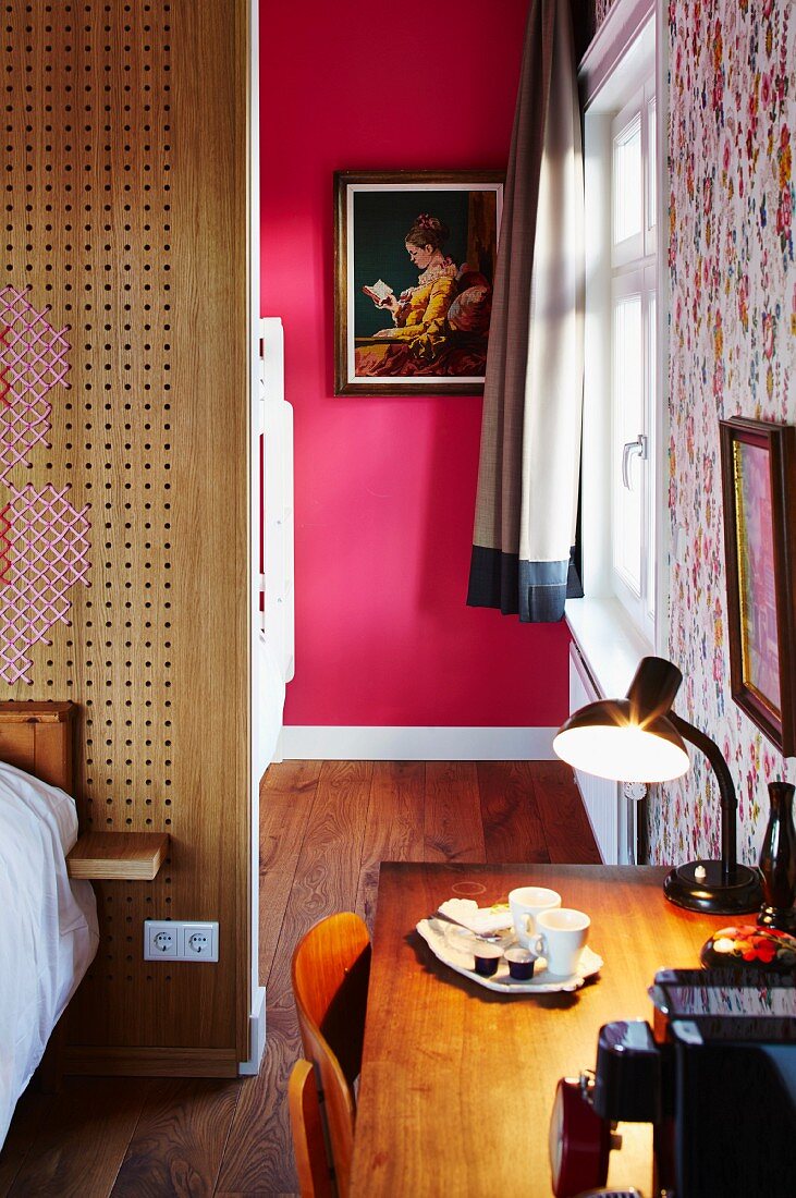 Desk in bedroom and view of artwork on hot pink wall seen through open doorway
