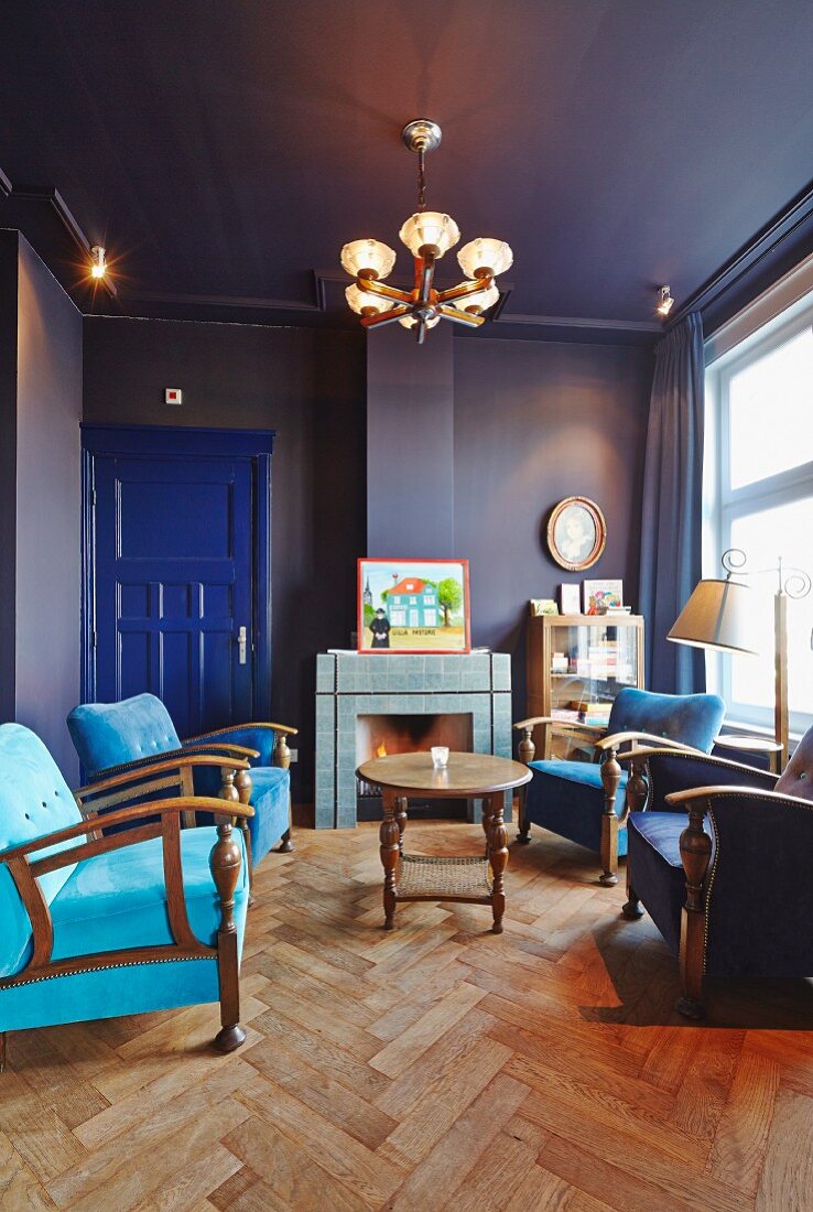 Blauer Salon mit Fischgrätparkett, Sesseln in verschiedenen Blautönen, im Hintergrund offener Kamin