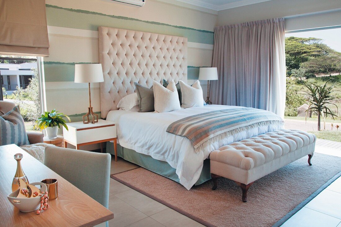 Elegantes Bett mit gepolstertem Kopfteil und Polsterbank vor offenem Schiebefenster