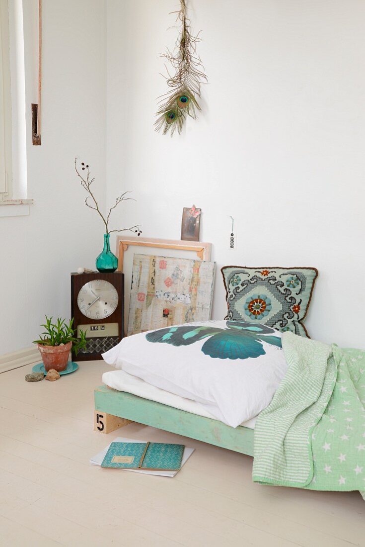 DIY-Tagesbett mit nostalgischem, gesticktem Kissen, Wanddeko mit Pfauenfedern und Retro Tischuhr in Zimmerecke