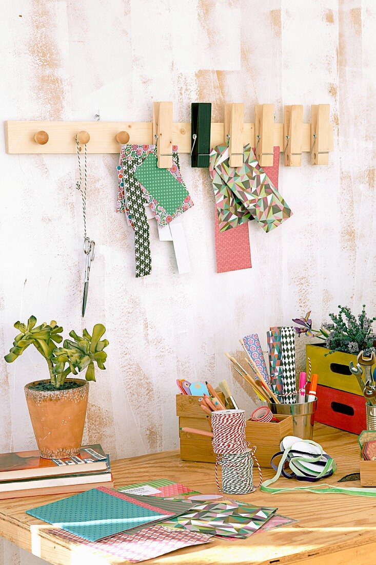 DIY-Wandleiste mit Möbelknöpfen und Holzklammern über Schreibtisch mit Bastelutensilien und Topfpflanze