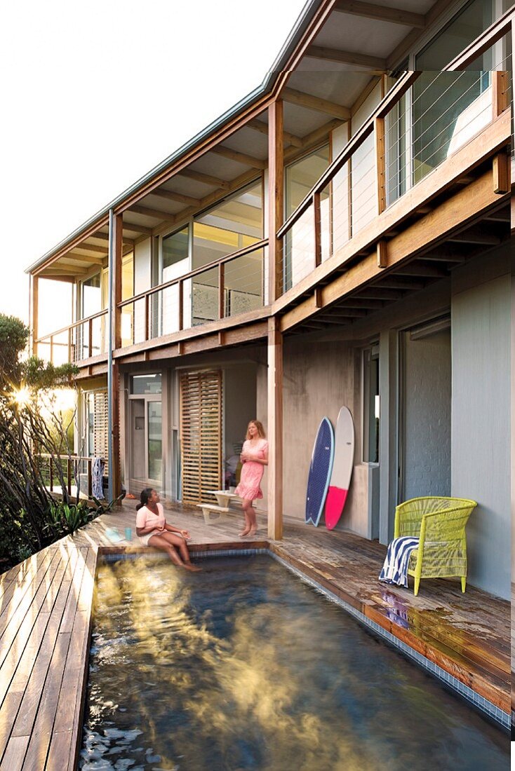 Pool integrated into wooden terrace outside house with timber-frame veranda and balcony