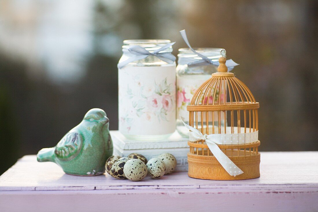 Romantisches Arrangement mit Wachteleiern, Vogelfigur, Miniatur-Vogelkäfig und verzierten Schraubgläsern