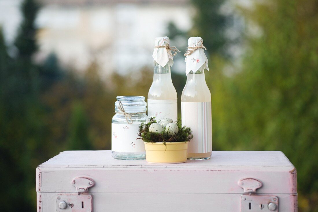 Osterdekoration: Deckelglas und Flaschen verziert mit Papier, Osternest mit Wachteleiern auf rosafarbenem Vintage-Koffer