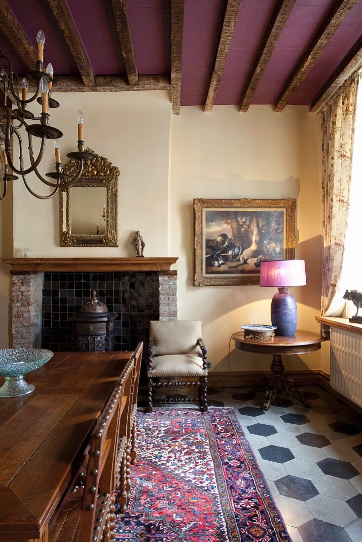 Tisch und Stühle mit gedrechselten Beinen auf Orientteppich in traditionellem Kaminzimmer, Holzbalken an violett getönter Decke