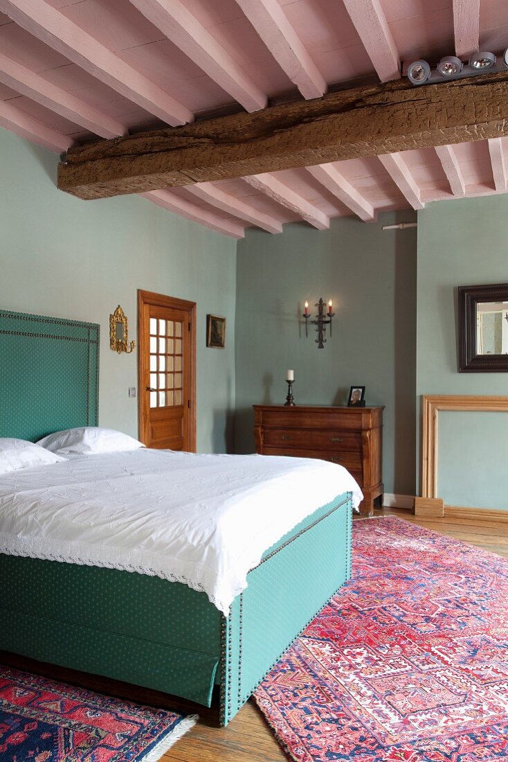 Double bed with turquoise upholstery and white bed linen in traditional bedroom with pink-painted wood-beamed ceiling and pastel turquoise walls