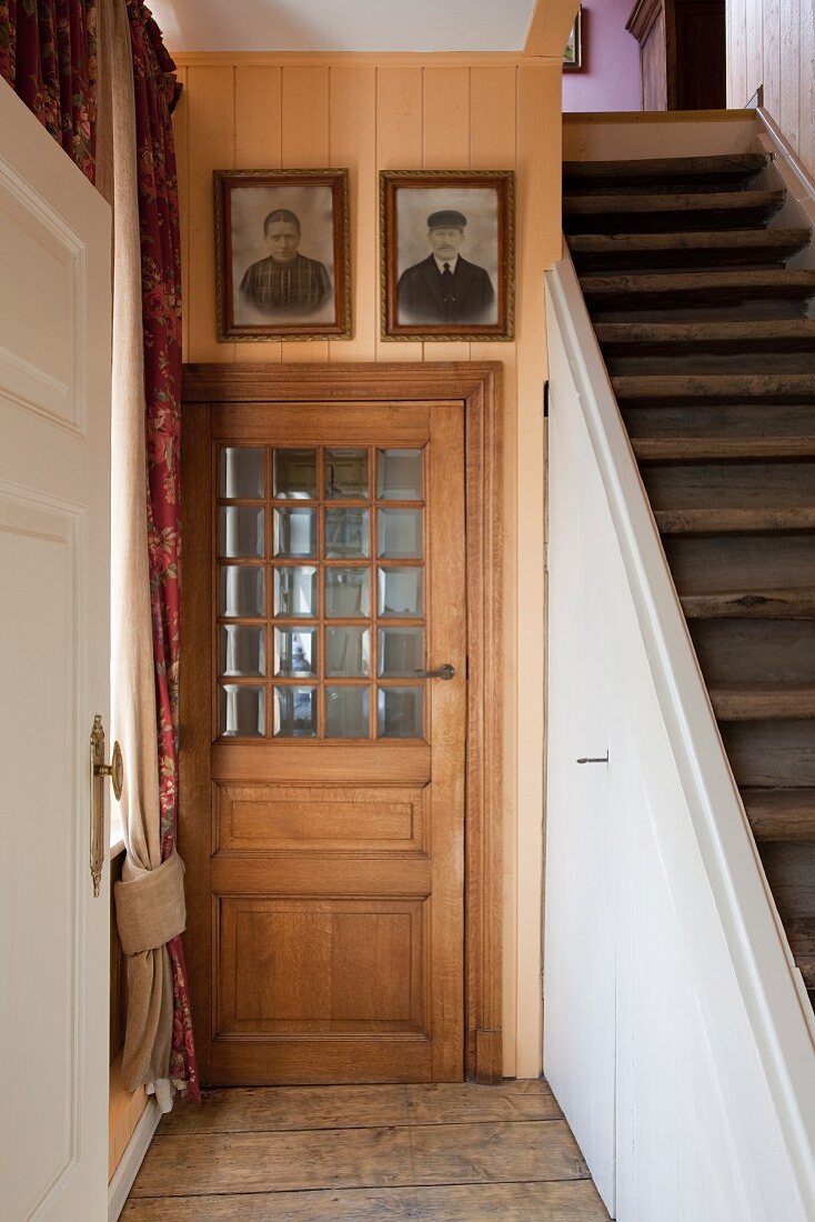 Traditional interior fittings: panelled wooden door with glass insert next to staircase with storage space below