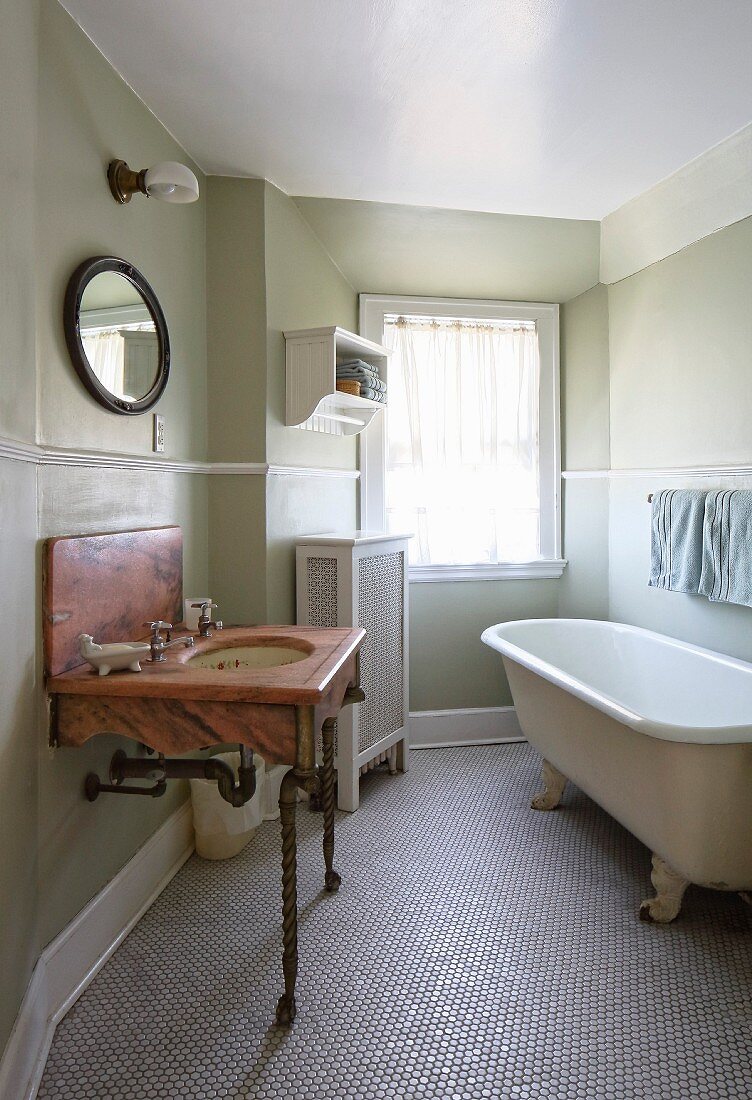 Marmor Waschtisch auf gedrechselten Metallfüssen und freistehende Vintage Badewanne auf Mosaikfliesen-Boden