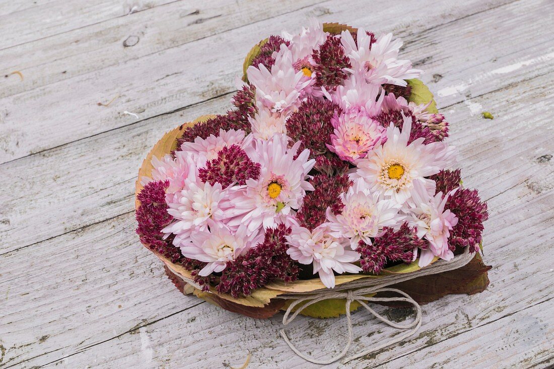 Herzförmig arrangiertes Gesteck aus Chrysanthemen und Herbstlaub