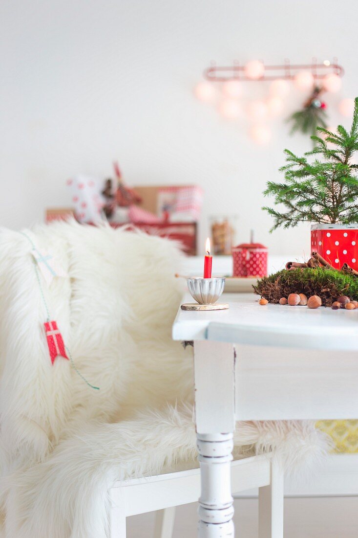 Stuhl mit weißem Fell neben Tisch mit Weihnachtsbäumchen und brennender Kerze