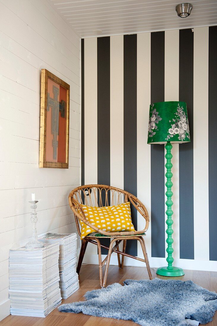 Rattanstuhl in Zimmerecke vor schwarz-weiss gestreifter Wand, und neben grüner Retro Stehleuchte