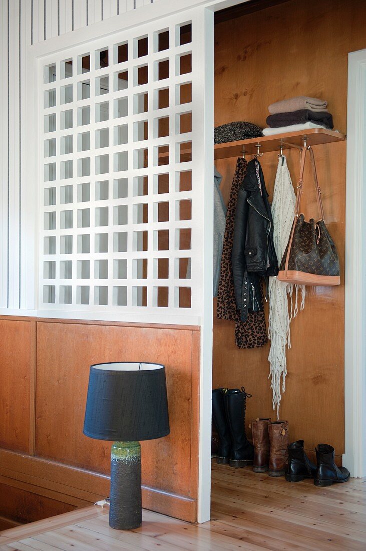 Tischleuchte mit schwarzem Lampenschirm auf Holzboden vor weißer Garderoben-Raumteilerwand am Treppenabgang