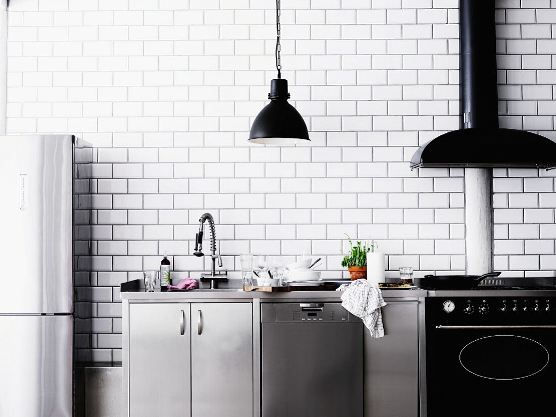 Modern kitchen counter in stainless steel and black against white-tiled wall