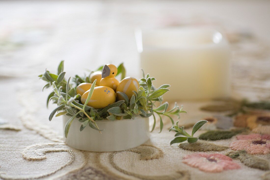 Bepflanztes Porzellangefäß als Osternest mit gelben Holzeiern und Kükenfigur