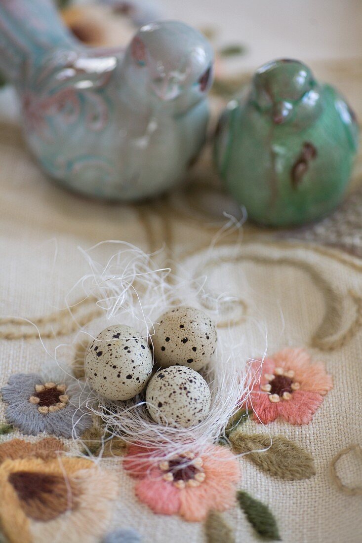 Quail eggs on white ornamental straw and turquoise bird ornaments on embroidered vintage tablecloth