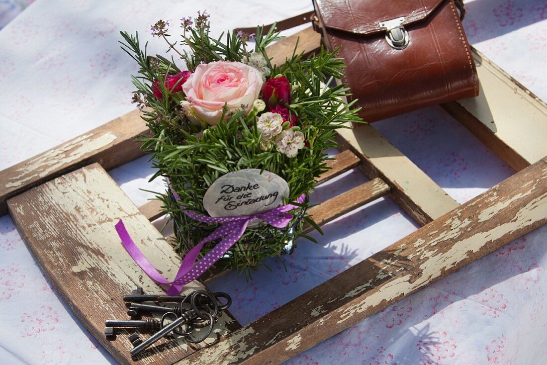 Arrangement of roses and herbs decorated with ribbon lying on detached backrest of old chair