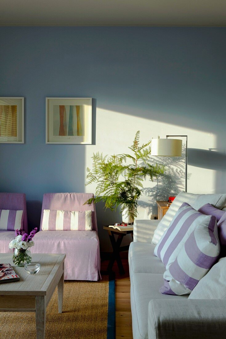 Sofa und Sessel mit pastellfarbenem Bezug und gestreifte Kissen im Wohnzimmer mit hellblauer Wand