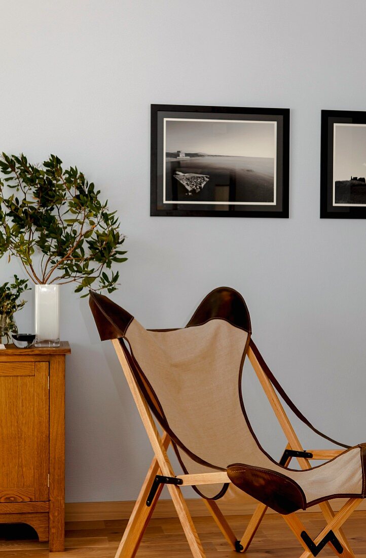 Sessel im Klassikerstil mit Holzgestell und Segelstoff Bezug, im Hintergrund gerahmte Fotos an hellblau getönter Wand
