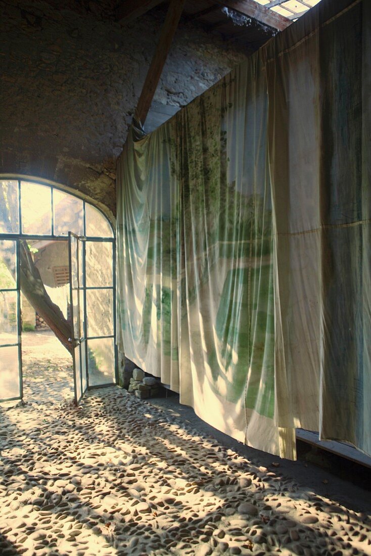 Sonneneinfall durch Rundbogenelement in alte Scheune, über Holzträger aufgehängte Tücher