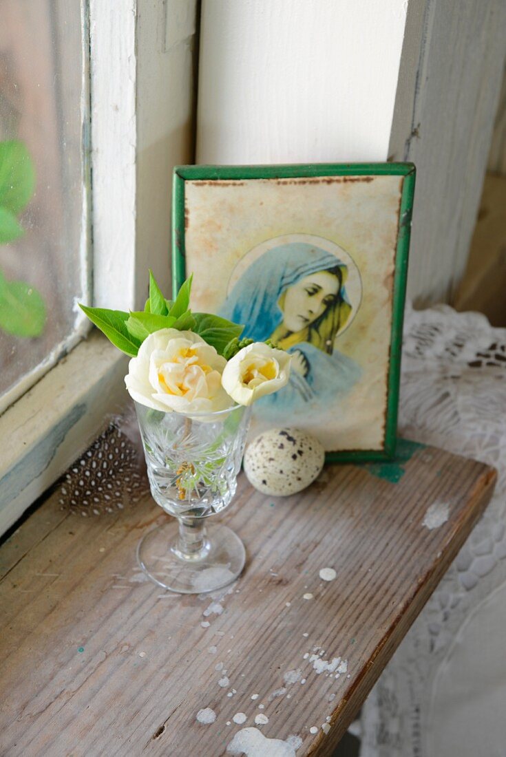 Kristallglas mit weißer Blüte auf Vintage Fensterbrett und Madonnenbild