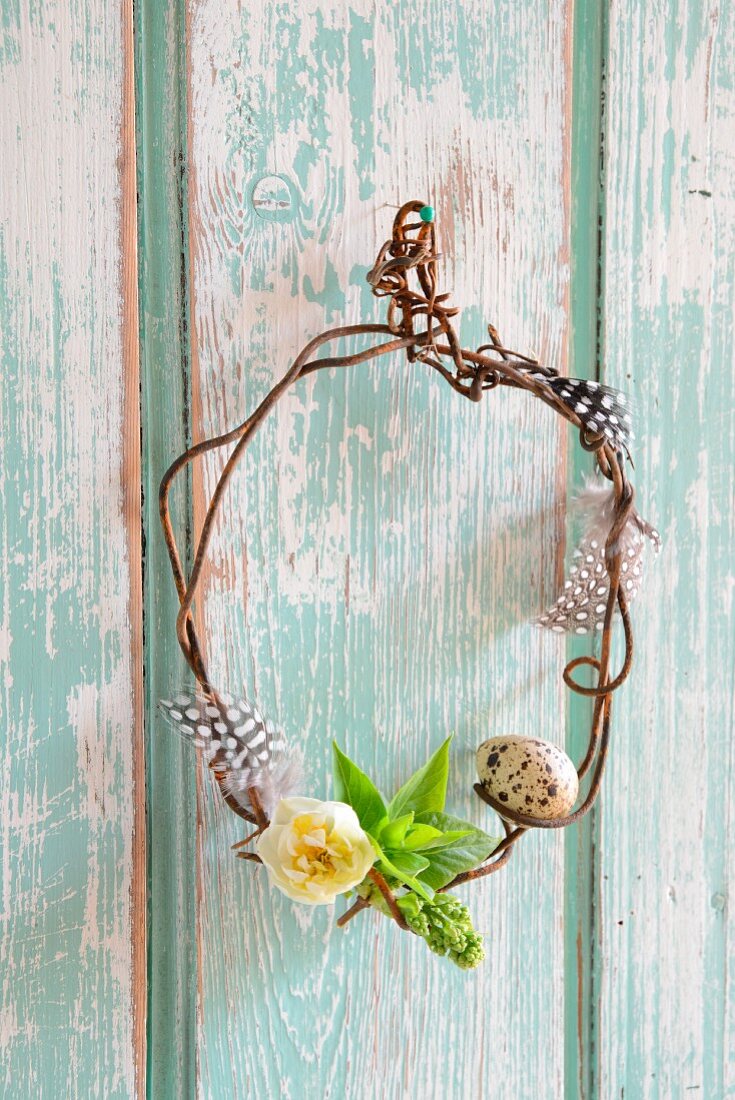 Small wreath of rusty wire decorated with quail egg, feathers and narcissus flower on wooden wall