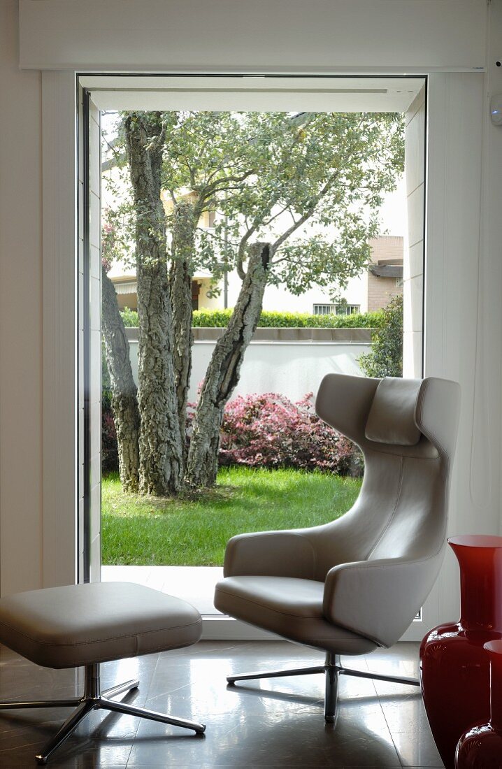 Designer easy chair with footstool by Antonio Citterio in front of window with garden view
