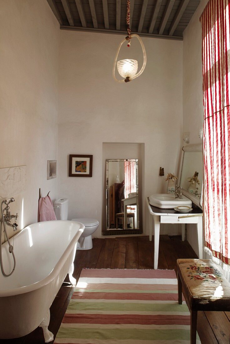 Free-standing vintage bathtub opposite window in rustic bathroom