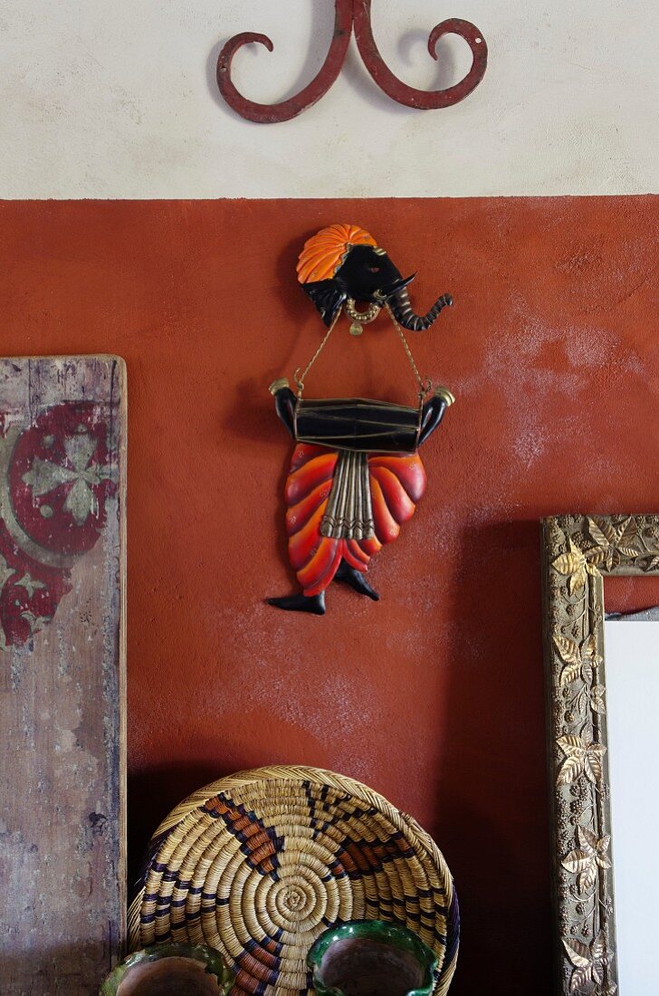 Fernöstliche Wanddekoration mit Elefantenfigur und kunsthandwerklicher Bastkorb an rotbrauner Wand