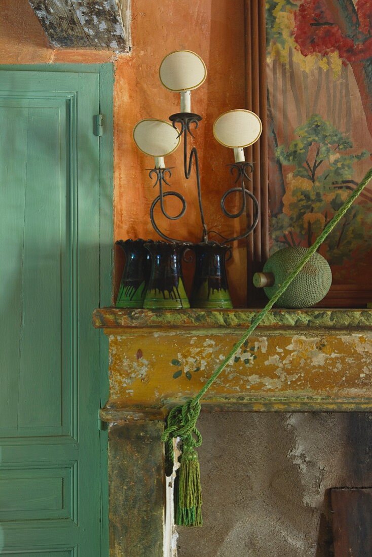 Kaminsims mit abblätternder Farbe, darauf Vasensammlung und Tischleuchte im Vintagestil
