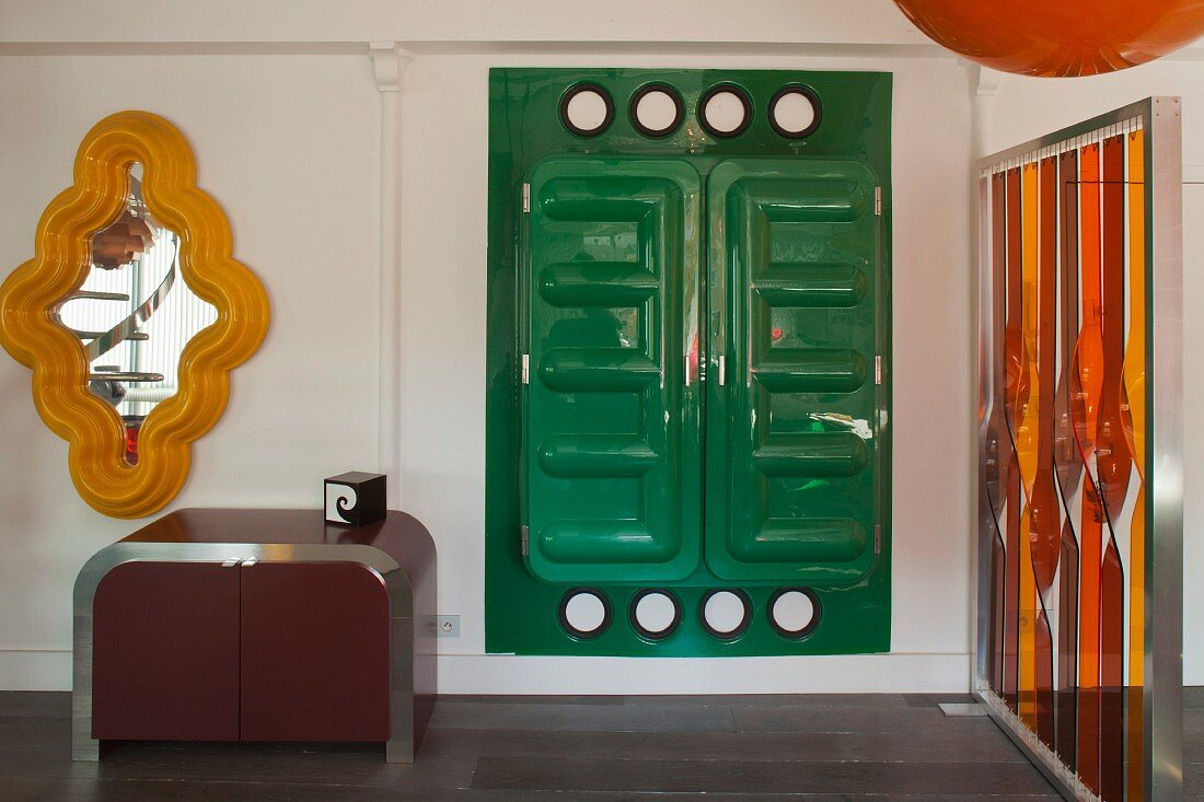 Postmodern occasional furniture, orange and red artwork, yellow-framed mirror and green plastic cupboard in pop-art interior