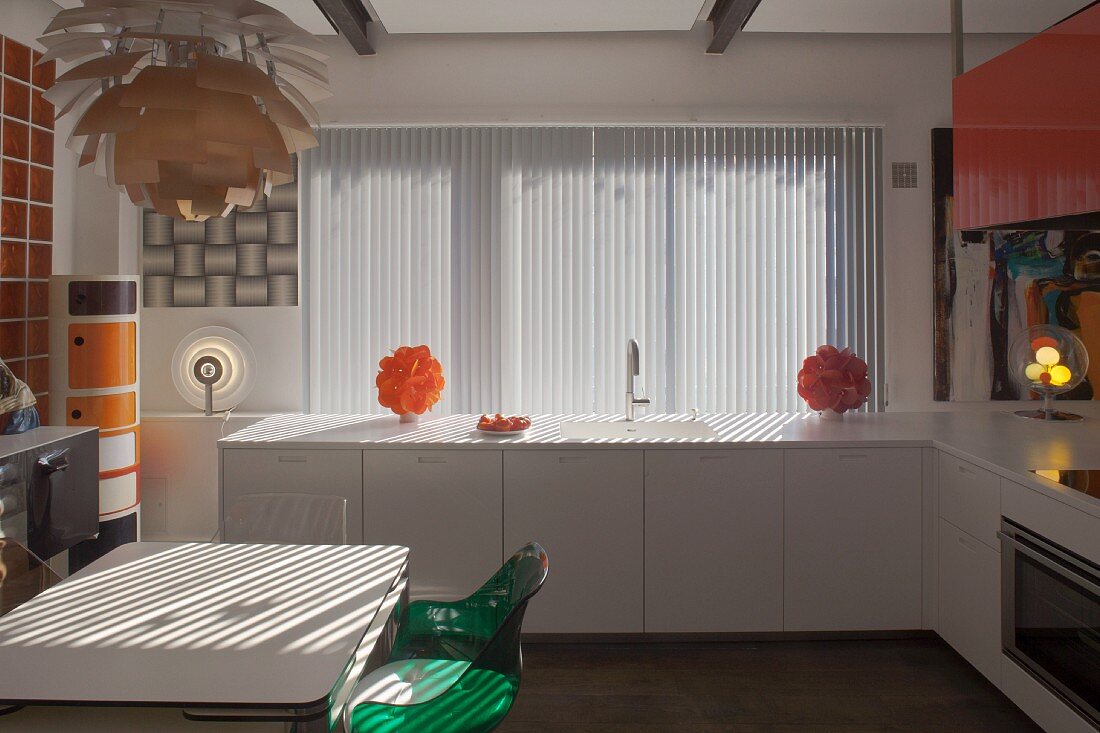 Essplatz unter Klassiker Pendelleuchte, moderne, weiße Küchenzeile vor Fenster mit Lamellenvorhang