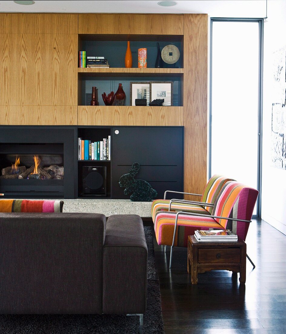 Striped armchairs, sofa and custom wooden cabinets against wall with integrated fireplace in living room
