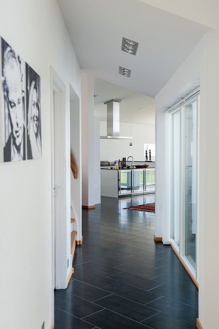 Gangbereich mit schwarzem Fliesenboden in Diagonalverlegung, im Hintergrund offen Küche