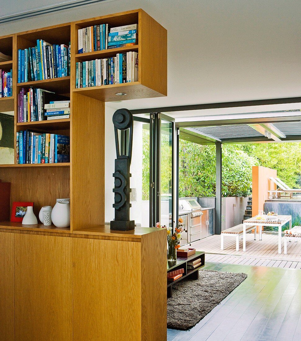 Fitted wooden cabinets as partition in modern interior with open folding sliding doors and view of terrace in background