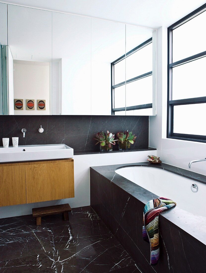 Zeitgenössisches Bad mit schwarzem Marmorfliesen auf Boden, im Hintergrund Spiegelschrank über Waschtisch